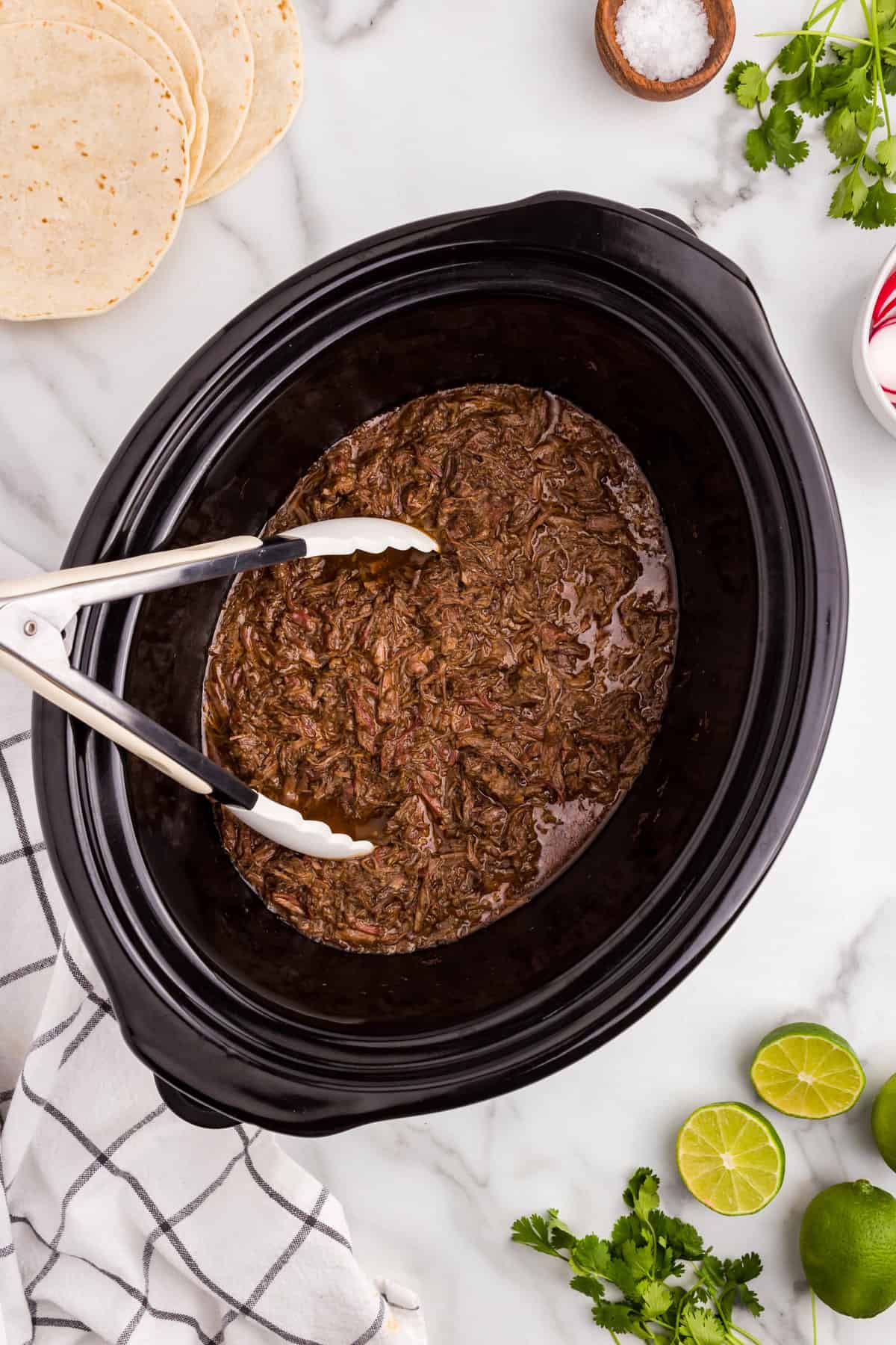 Beef Barbacoa shredded and cooked in crock pot with serving tongs