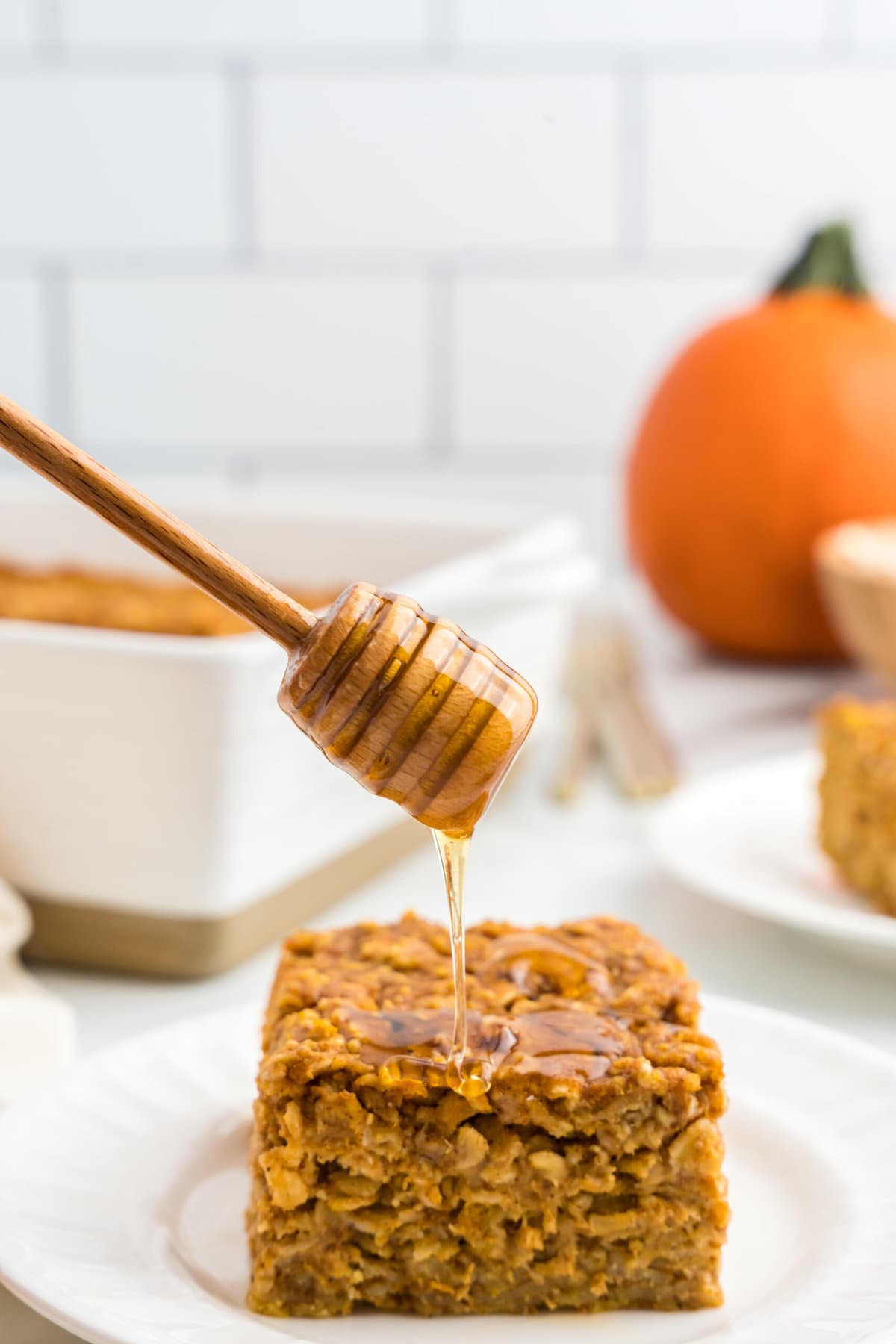 Pumpkin Baked Oatmeal square on plate being drizzled with honey