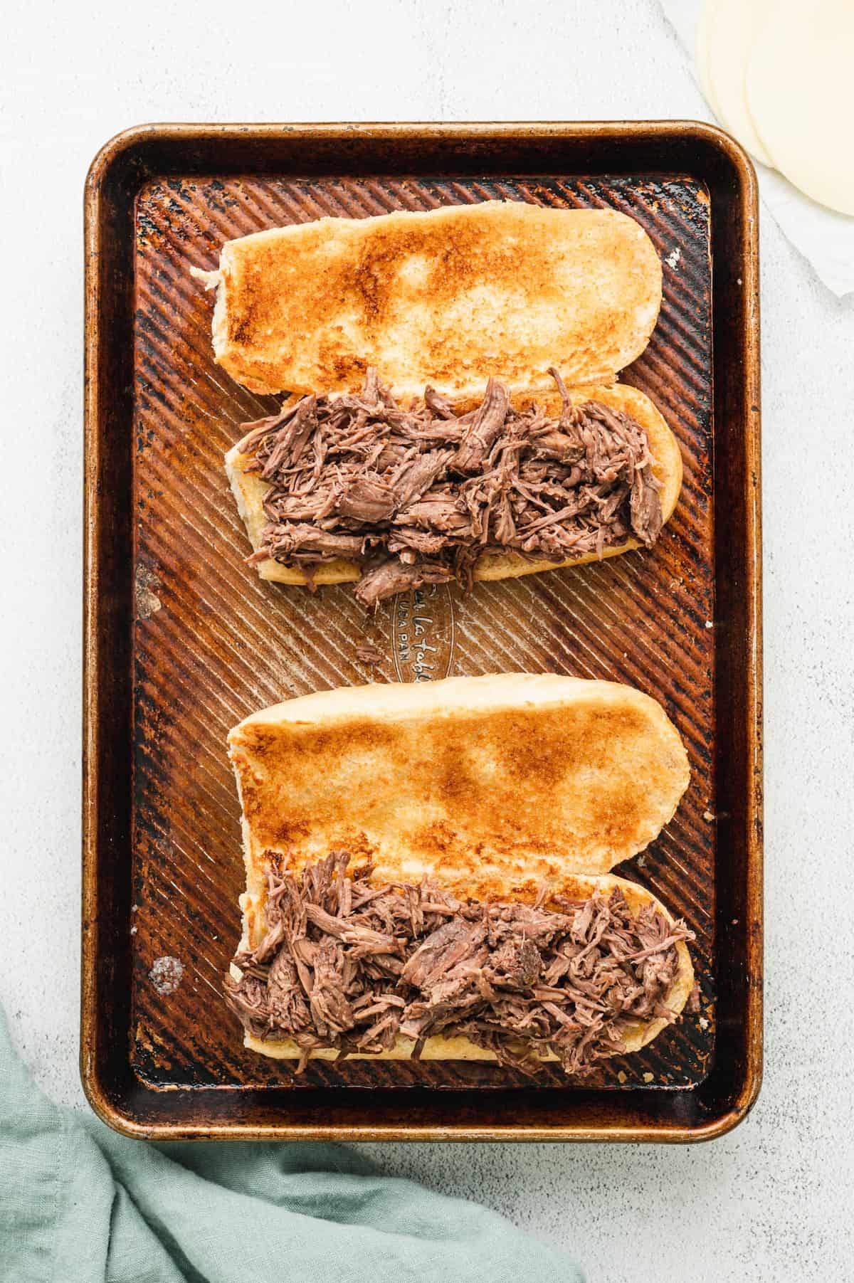 Adding shredded seasoned beef to open faced toasted hoagies for French Dip