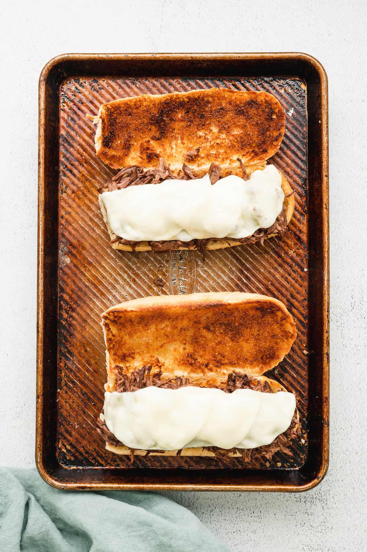 Meling provolone cheese atop meat on open faced toasted hoagies for French Dip Sandwiches. 