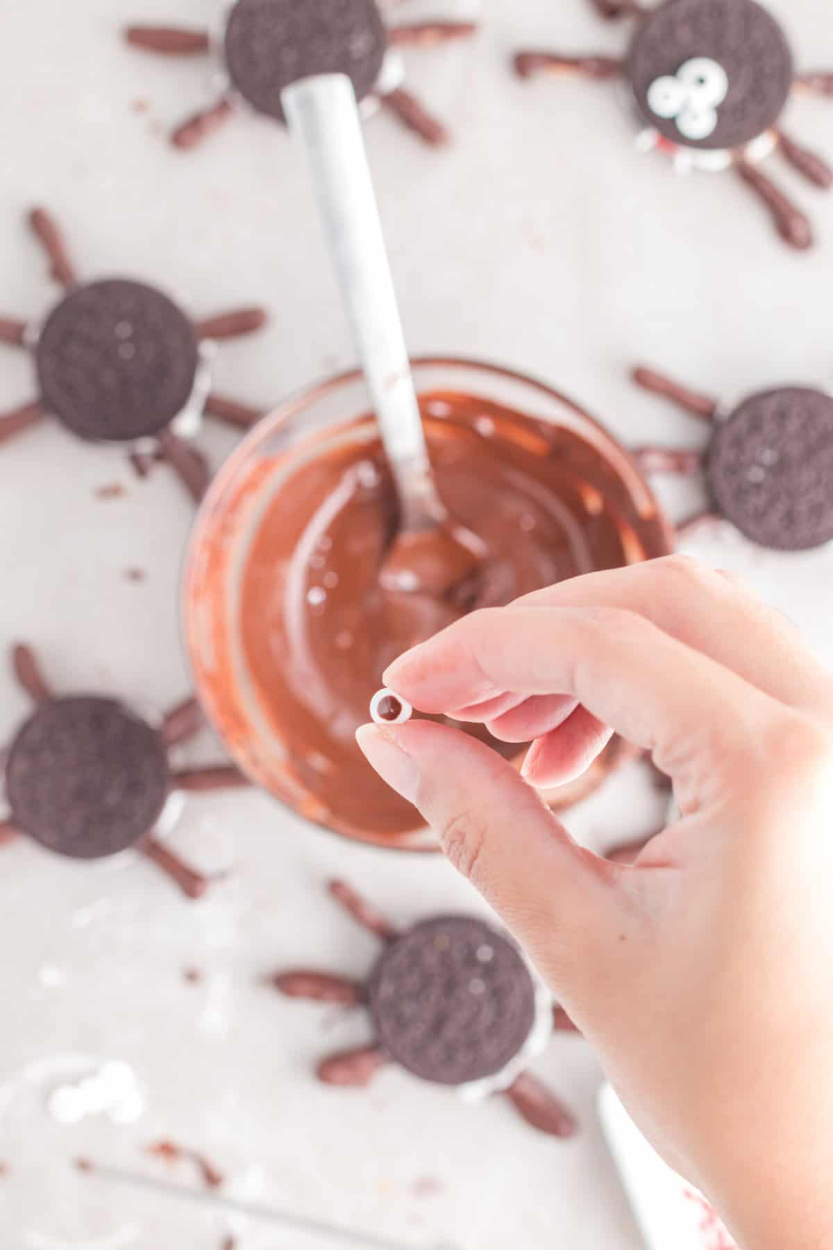 Using the melted chocolate to attach the eyes to the top of the Spider Cookie