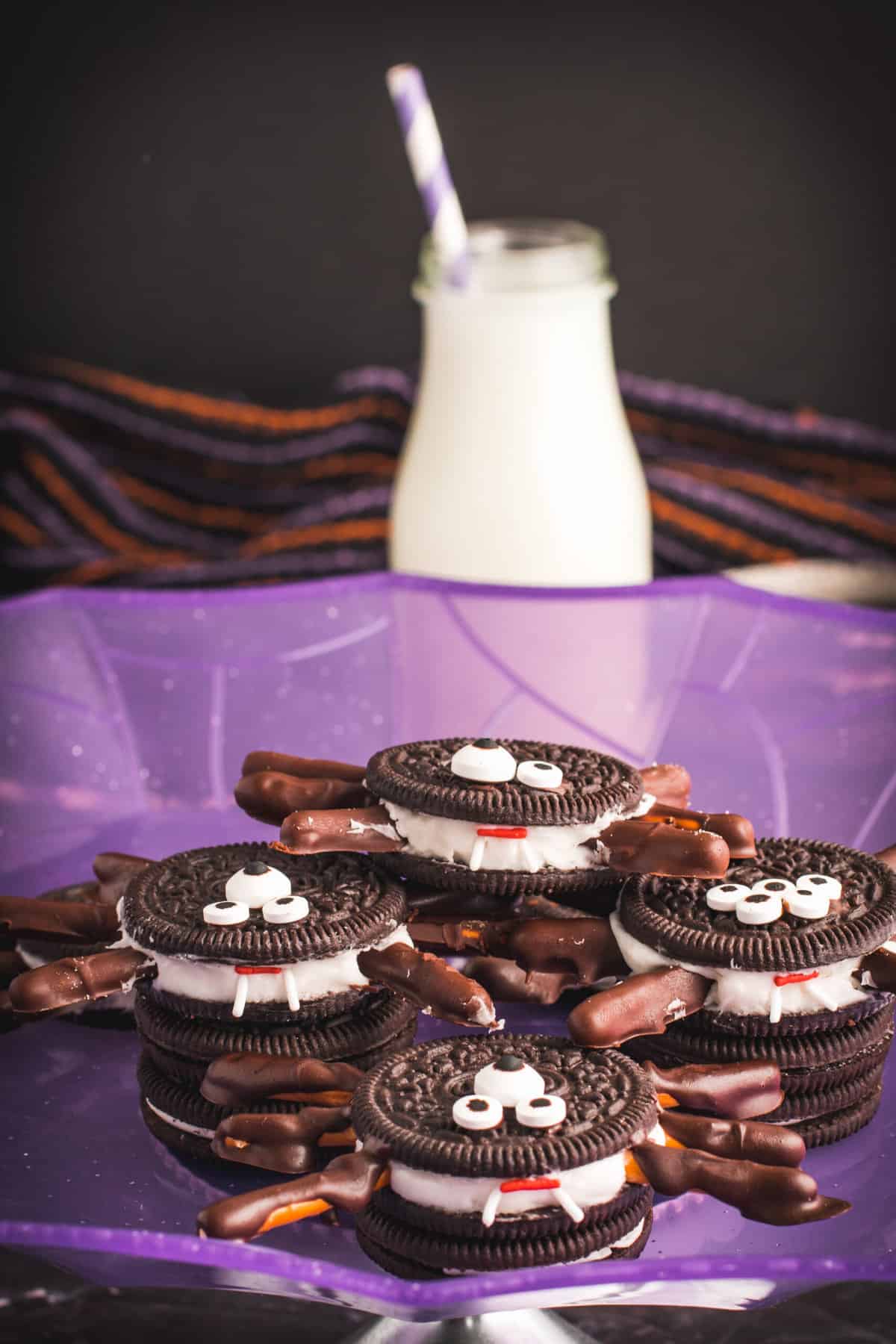 Oreo Spider cookies in the purple spider web plate with a glass of milk behind.