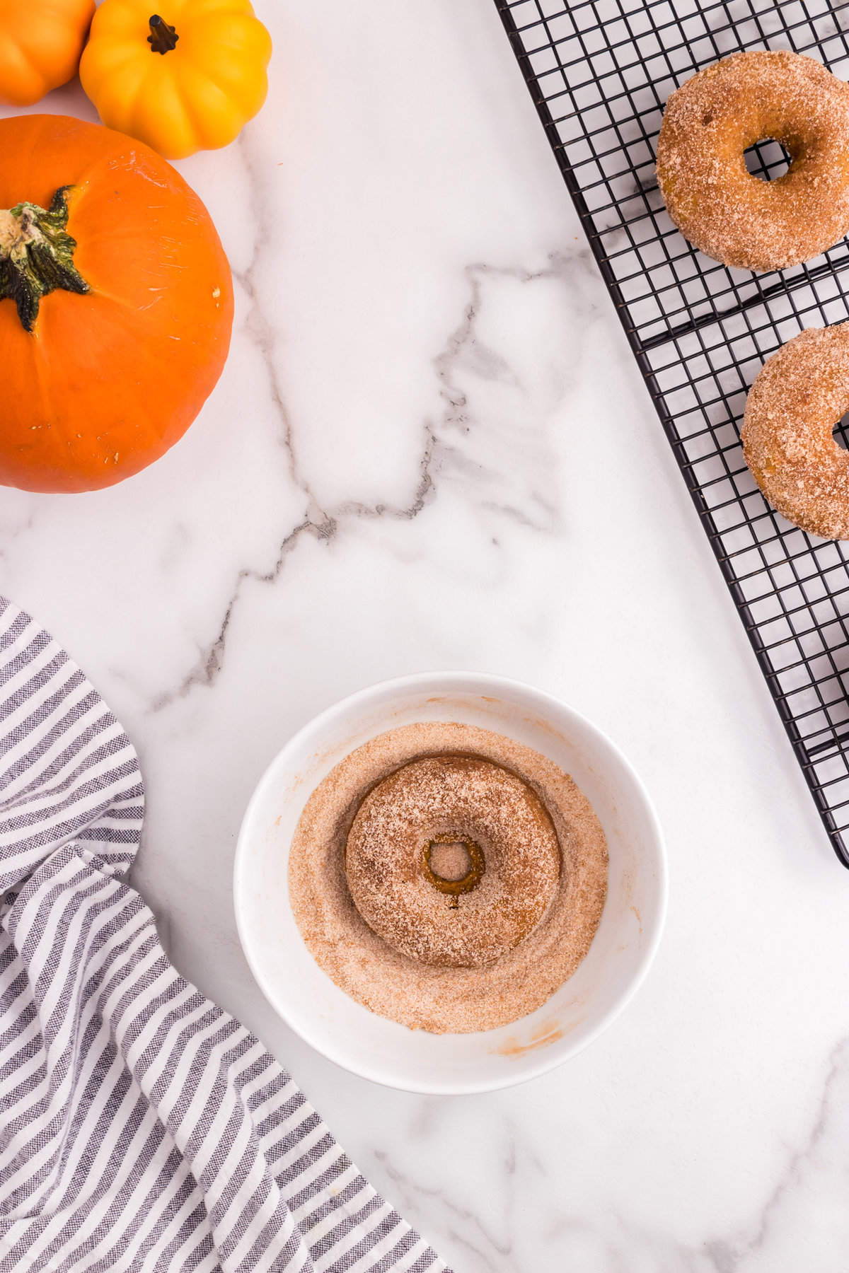 Coating Pumpkin Donuts in cinnamon and sugar mixture in shallow bowl