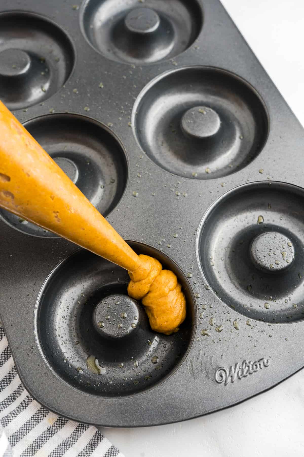 Piping Pumpkin Donuts batter into prepared donut tin