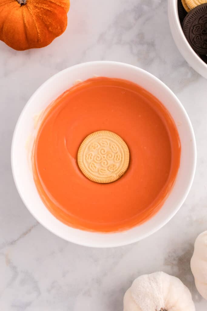 Take a cookie and completely dunk it into the bowl of orange white chocolate.