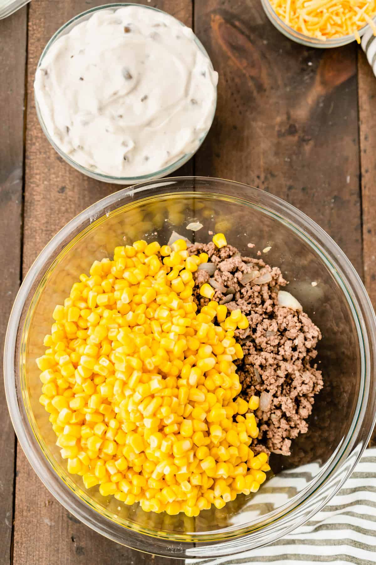 Adding canned corn to ground beef mixture in bowl for Tator Tot Hotdish recipe