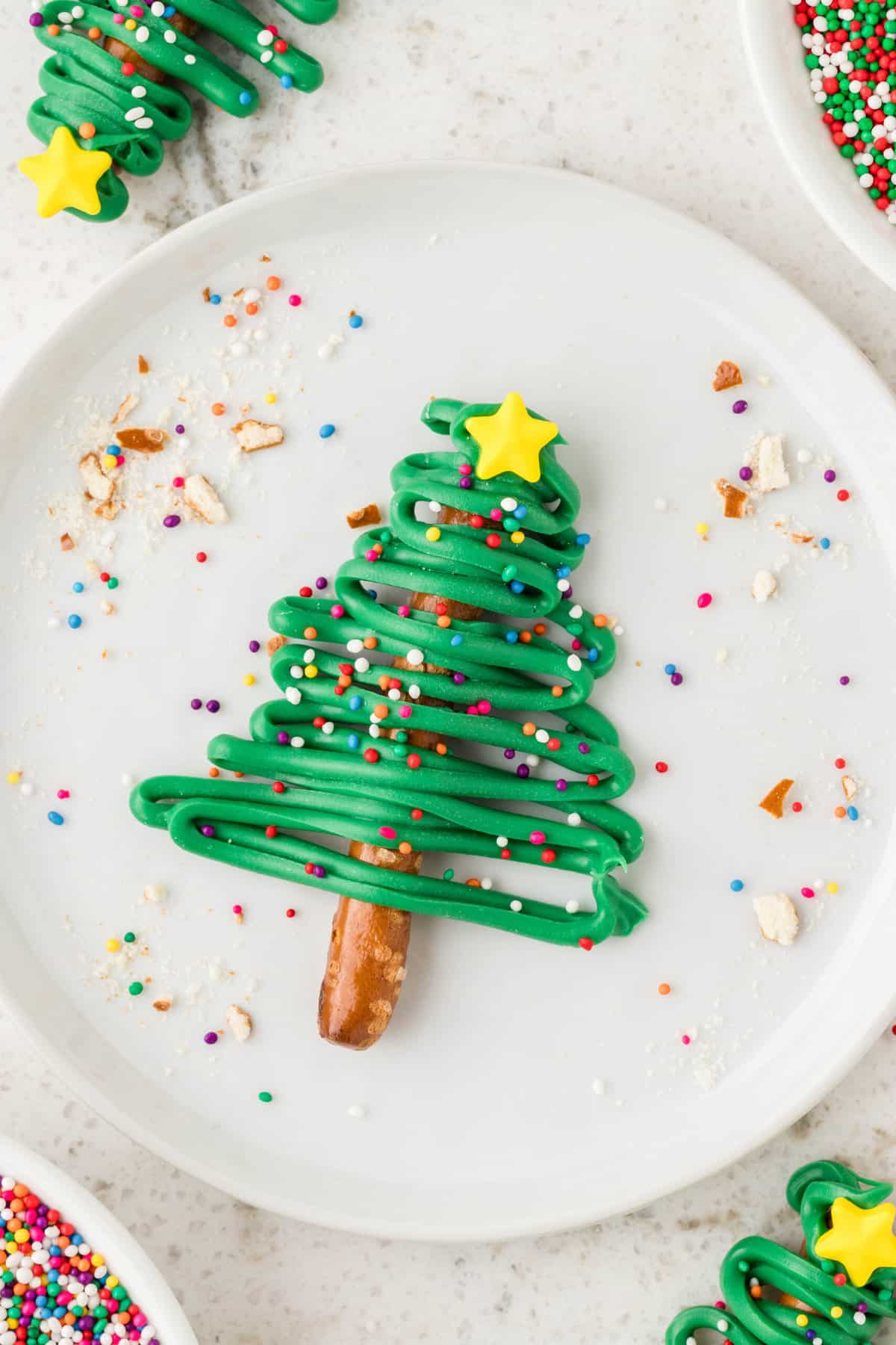 One Christmas Tree Pretzel displayed on a white plate with sprinkles around it.