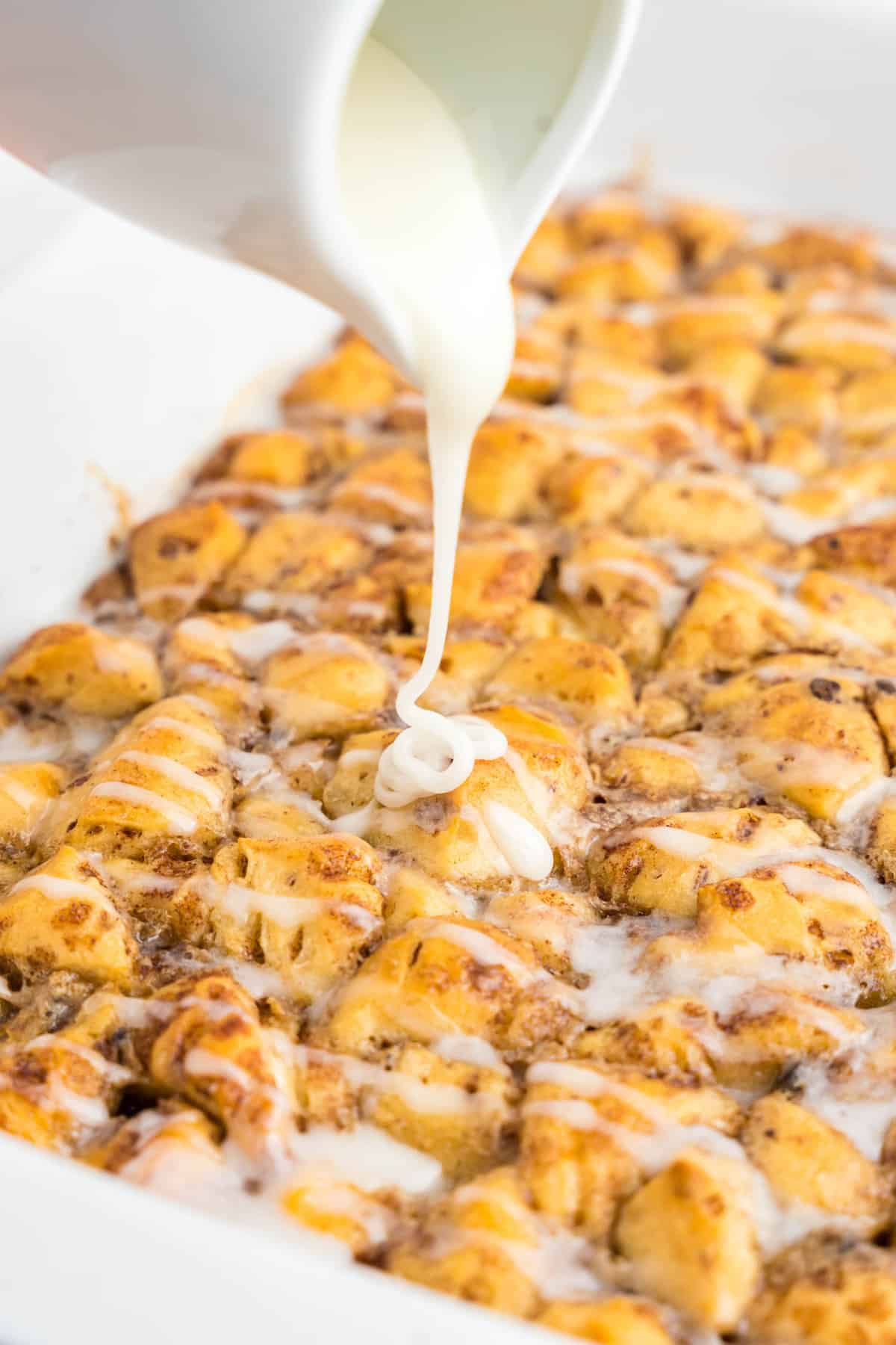 Pouring frosting over Cinnamon Roll Casserole in baking dish