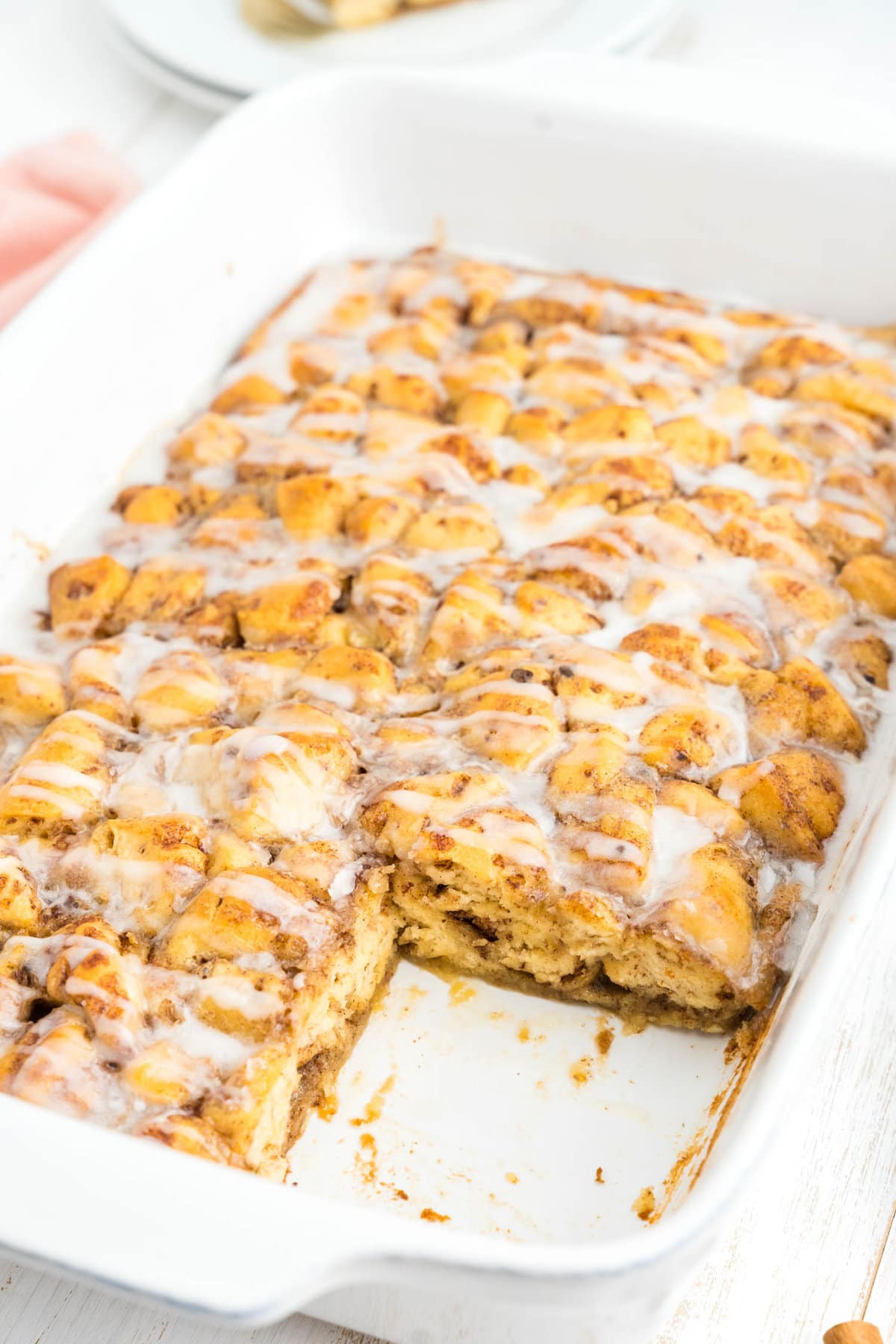 Cutting Cinnamon Roll Casserole into squares, with one already removed from baking dish