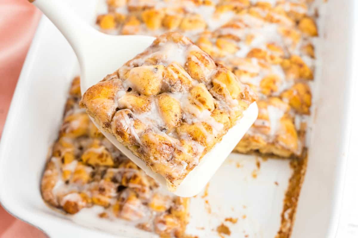Using a spatula to scoop a Cinnamon Roll Casserole square from baking dish