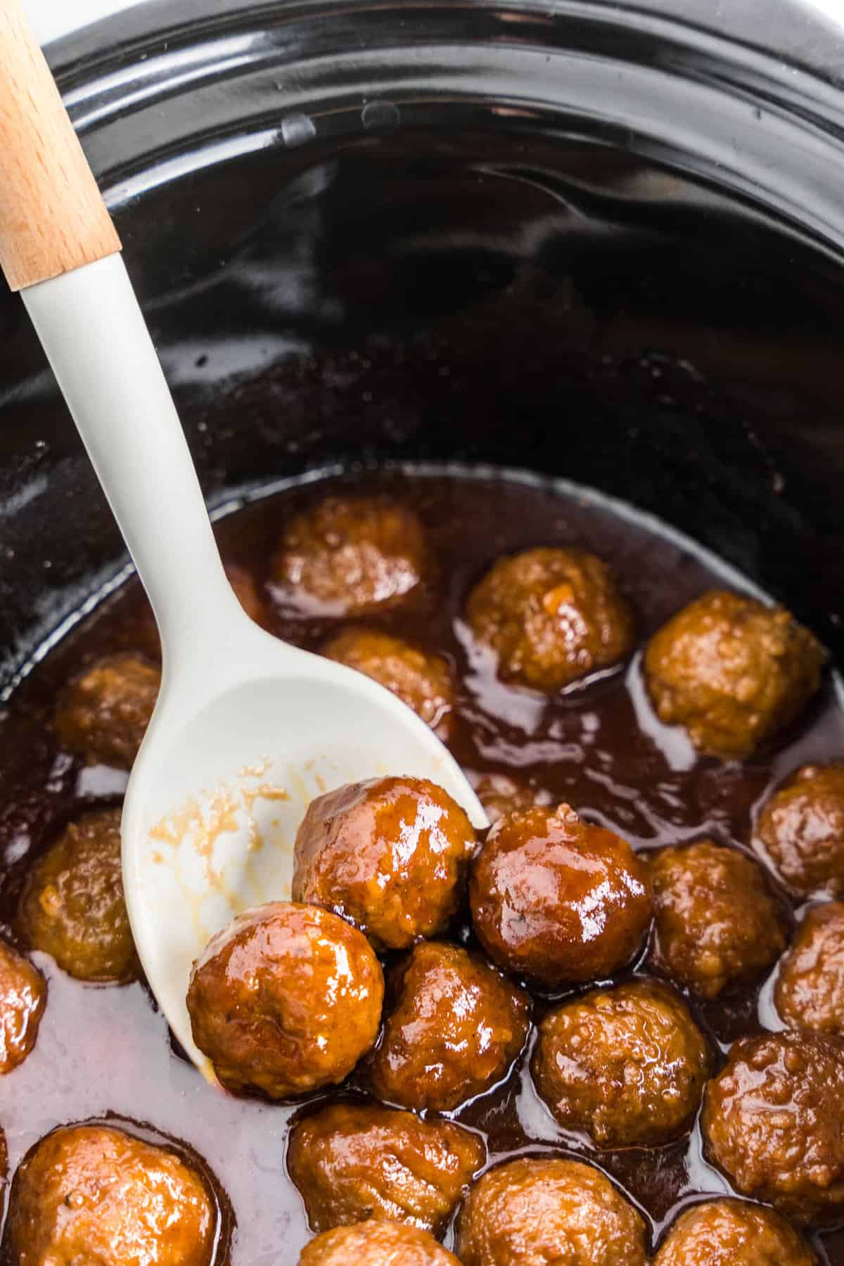 Stirring Grape Jelly Meatballs with spoon in crock pot