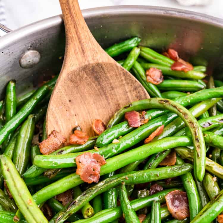 Green Beans with Bacon in stovetop skillet using wood spoon to toss