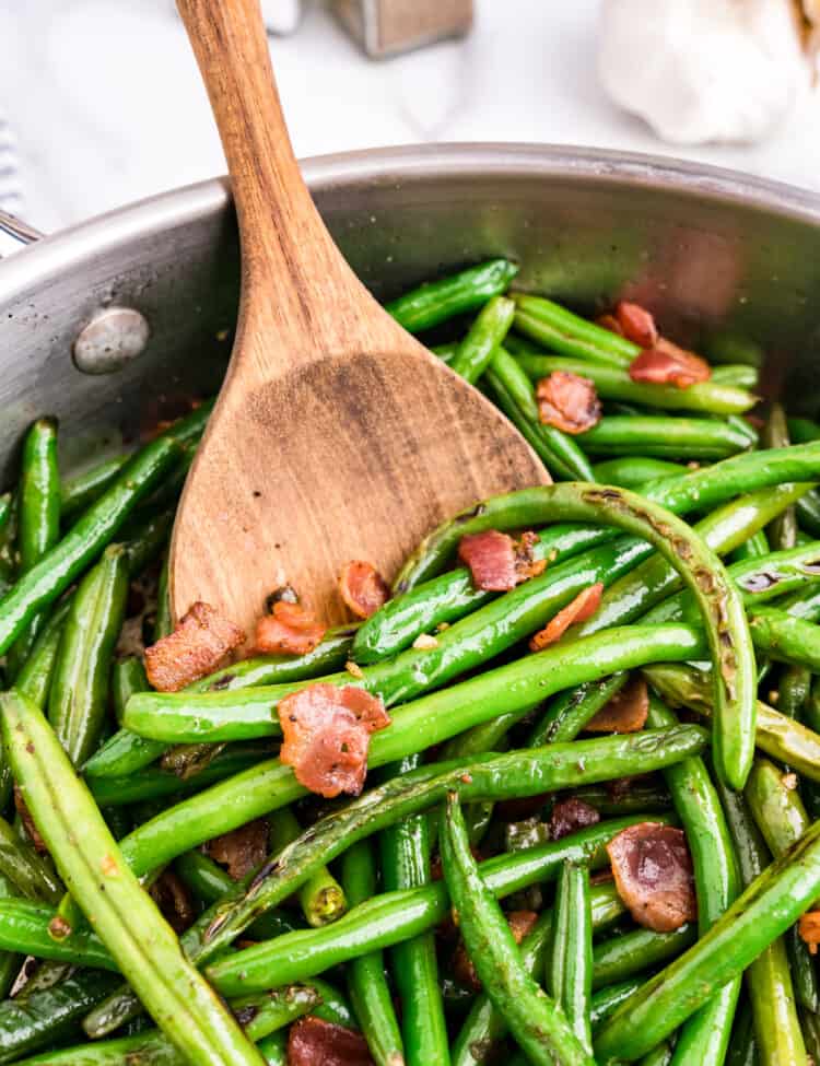 Green Beans with Bacon in stovetop skillet using wood spoon to toss