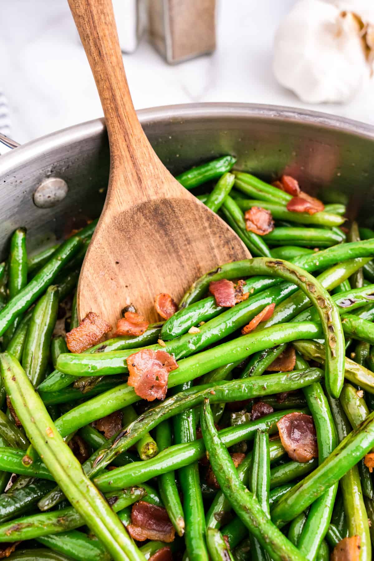 Green Beans with Bacon in stovetop skillet using wood spoon to toss
