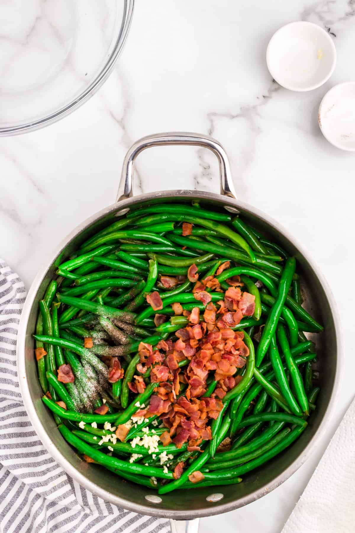 Adding cooked bacon, garlic, and seasonings to green beans in skillet for Green Beans with Bacon recipe