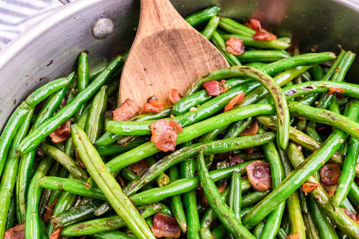 Bacon Green Beans being tossed with wooden spoon in stovetop skillet