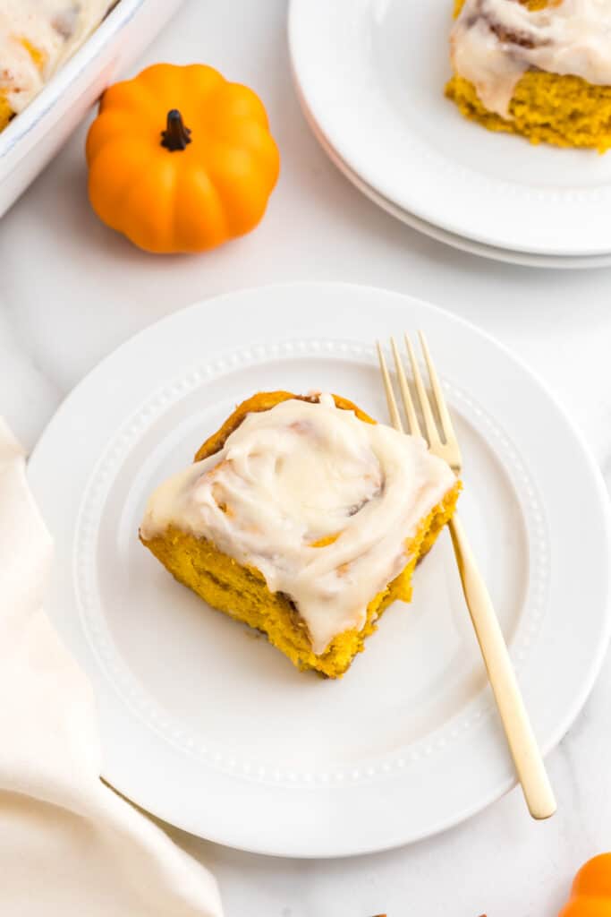 Pumpkin Spice Cinnamon Roll covered with cream cheese frosting on plate with fork