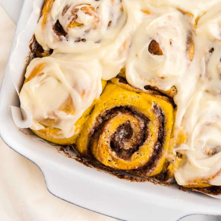 Closeup Square Image of Pumpkin Cinnamon Rolls in baking dish with one unfrosted roll