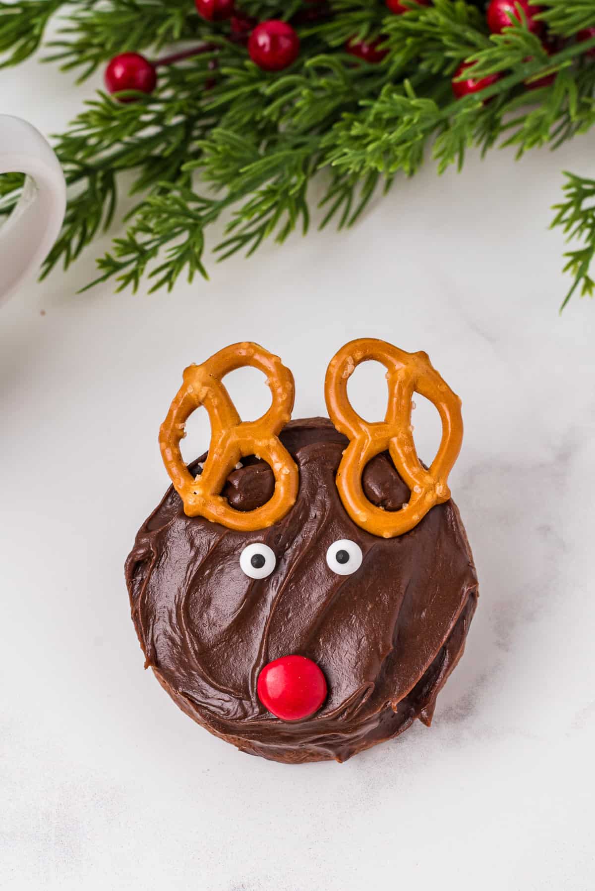 Close up photo of one reindeer cookie with greenery above it.