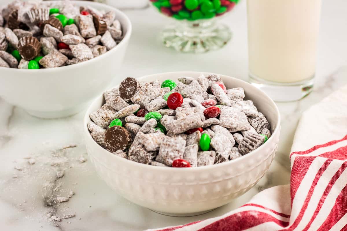 Two white bowls full of Reindeer chow with a glass of milk in the background.