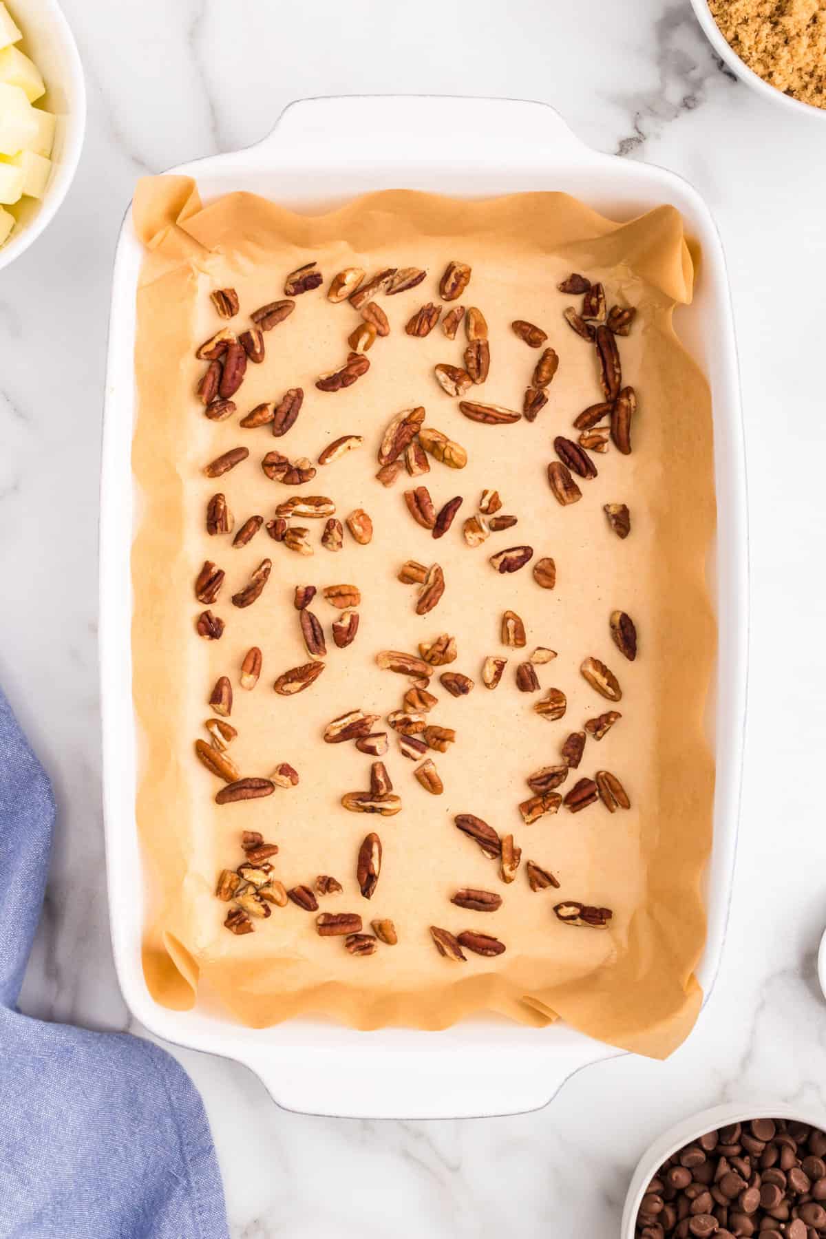 Tossing pecans over parchment paper in baking dish for Homemade Toffee recipe