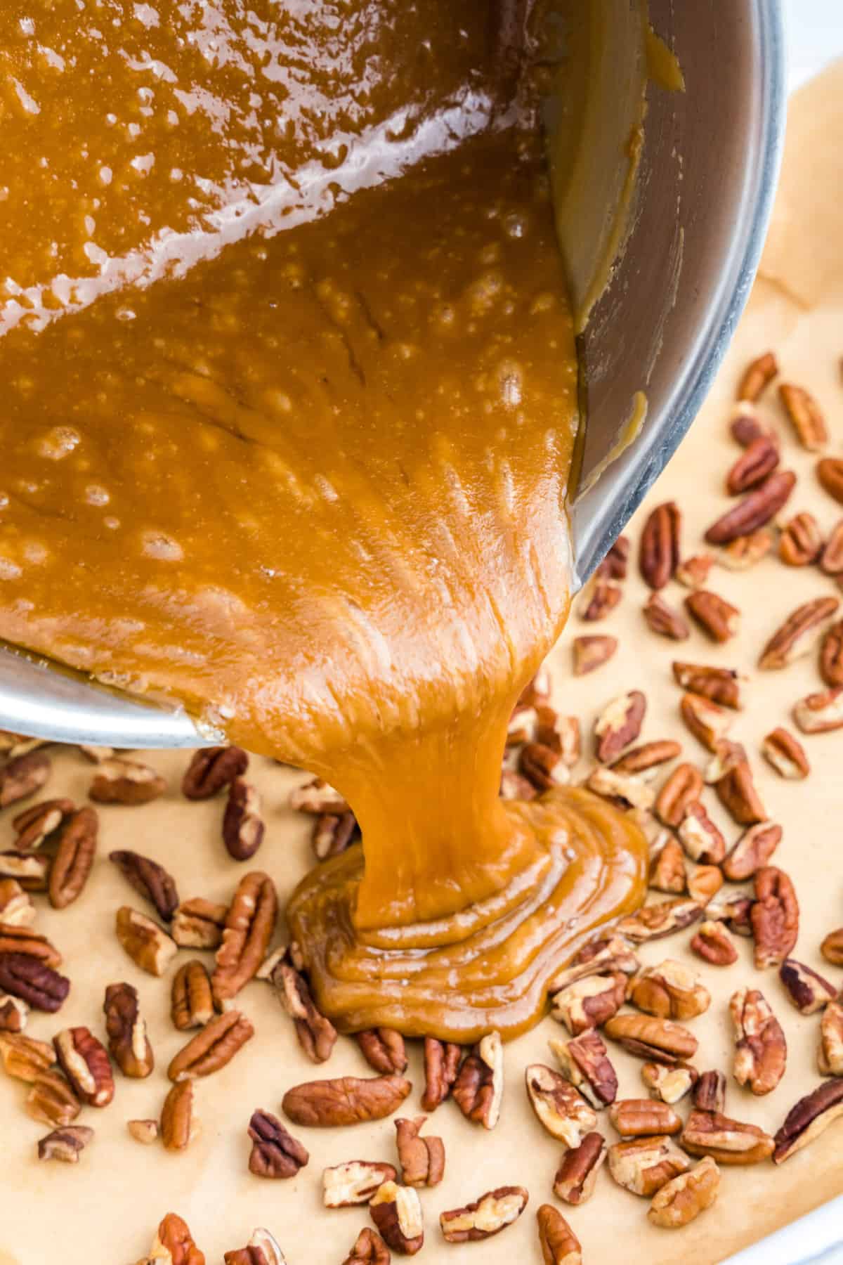 Pouring Toffee mixture over pecans in parchment-lined baking dish