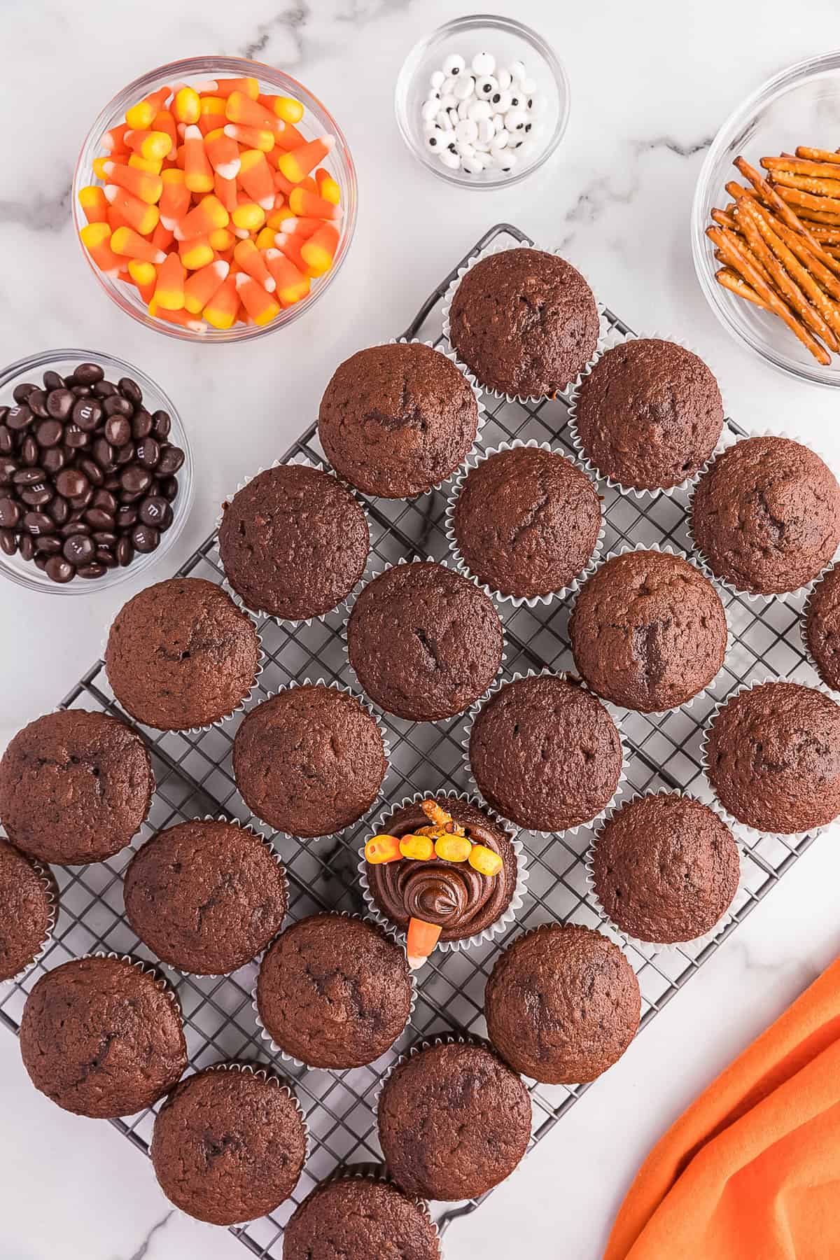 Then place 4 candy pieces in front of the two pretzels with the points pressing down into the frosting. Place another candy corn in the front of the cupcake with the tip facing outward for a beak.