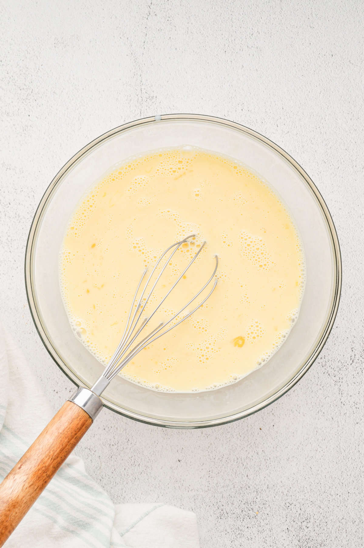 Whisking together eggs and milk for Bicuits & Gravy Casserole egg mixture in glass bowl