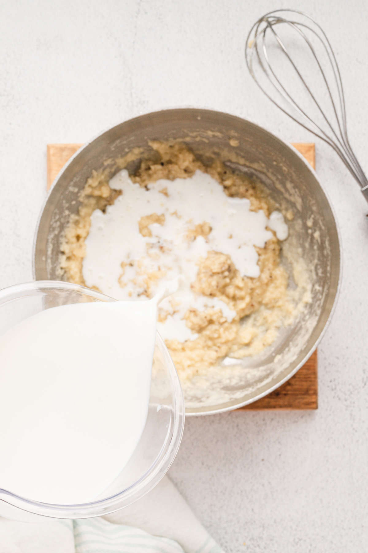 Pouring in milk to gravy mixture for Bicuits & Gravy Casserole recipe in stovetop saucepan