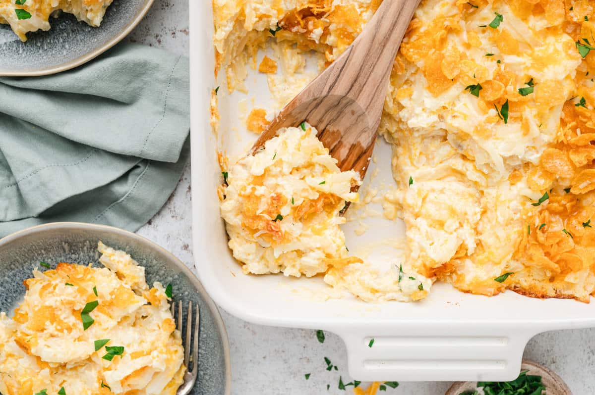 Funeral Potatoes in baking dish using a wooden spoon to scoop out