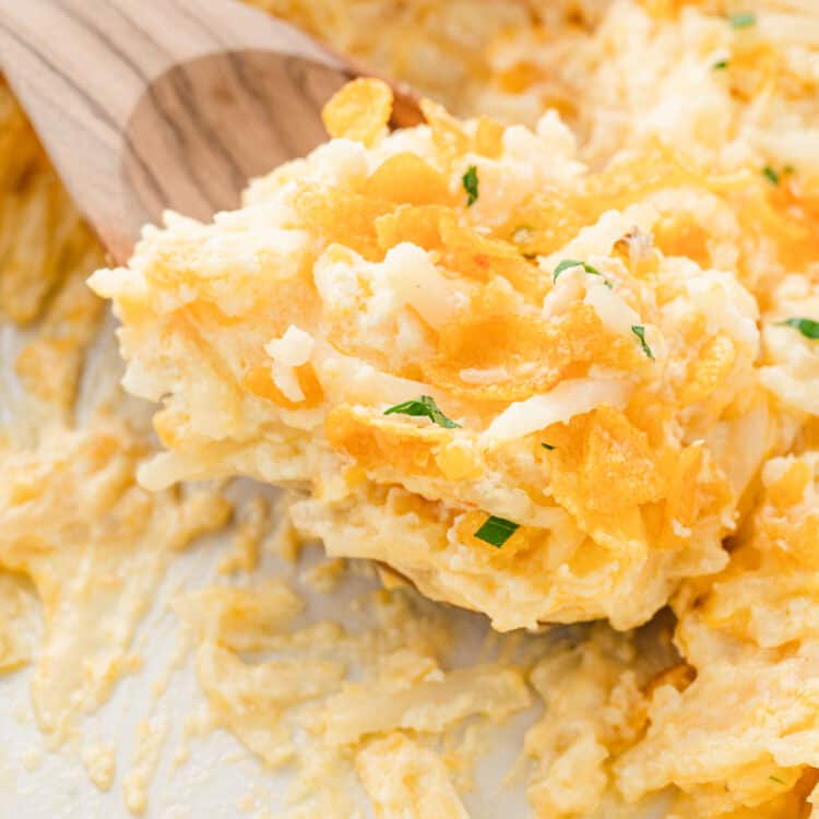 Closeup image of Funeral Potatoes being scooped from baking dish with wooden spoon