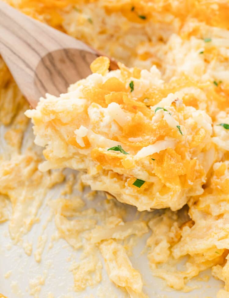 Closeup image of Funeral Potatoes being scooped from baking dish with wooden spoon
