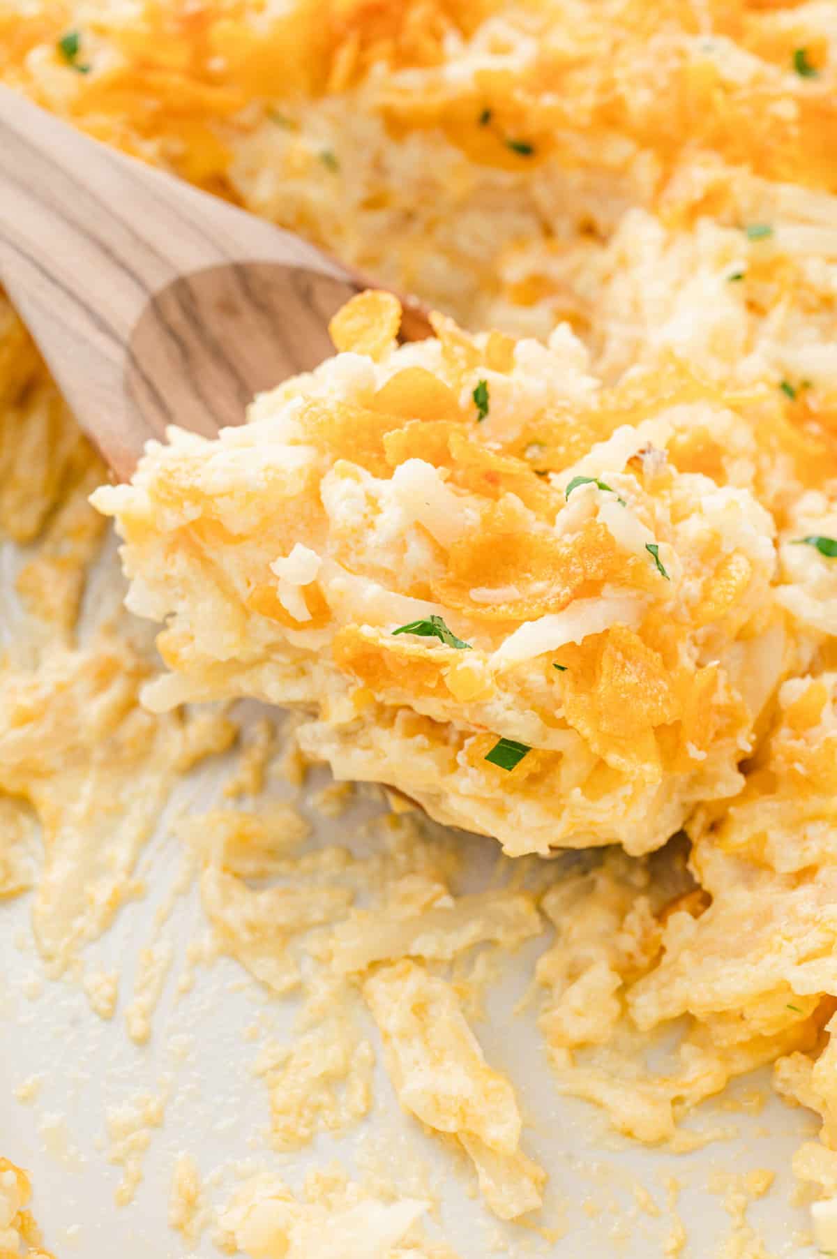 Closeup image of Funeral Potatoes being scooped from baking dish with wooden spoon