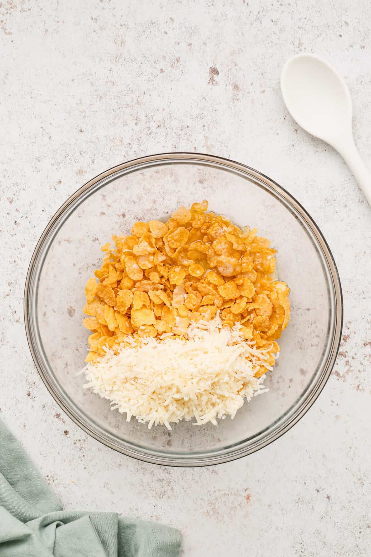 Cornflakes, melted butter, and Parmesan cheese in glass mixing for Funeral Potatoes recipe