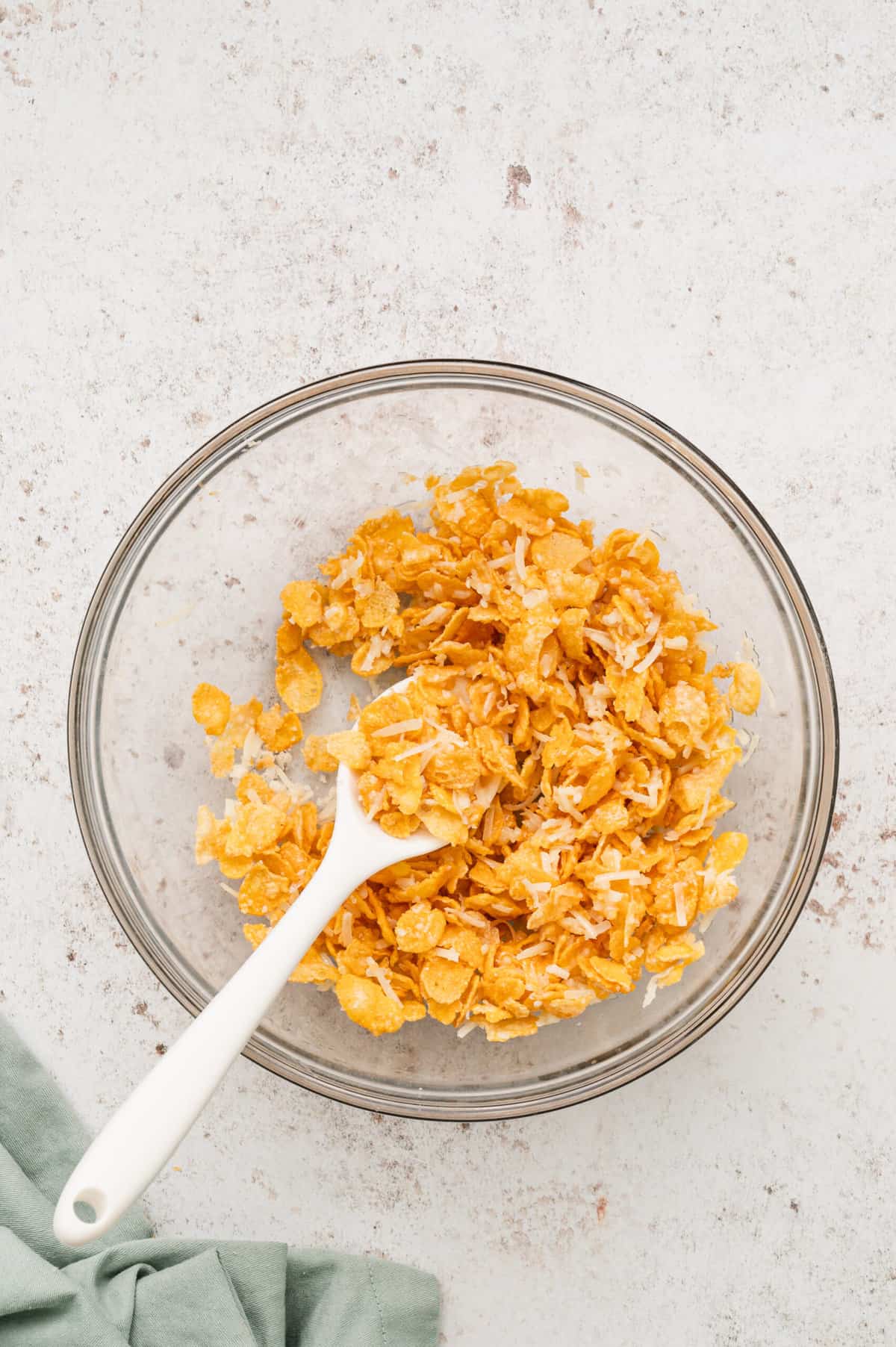 Combined cornflakes, melted butter, and Parmesan cheese in glass mixing for Funeral Potatoes recipe