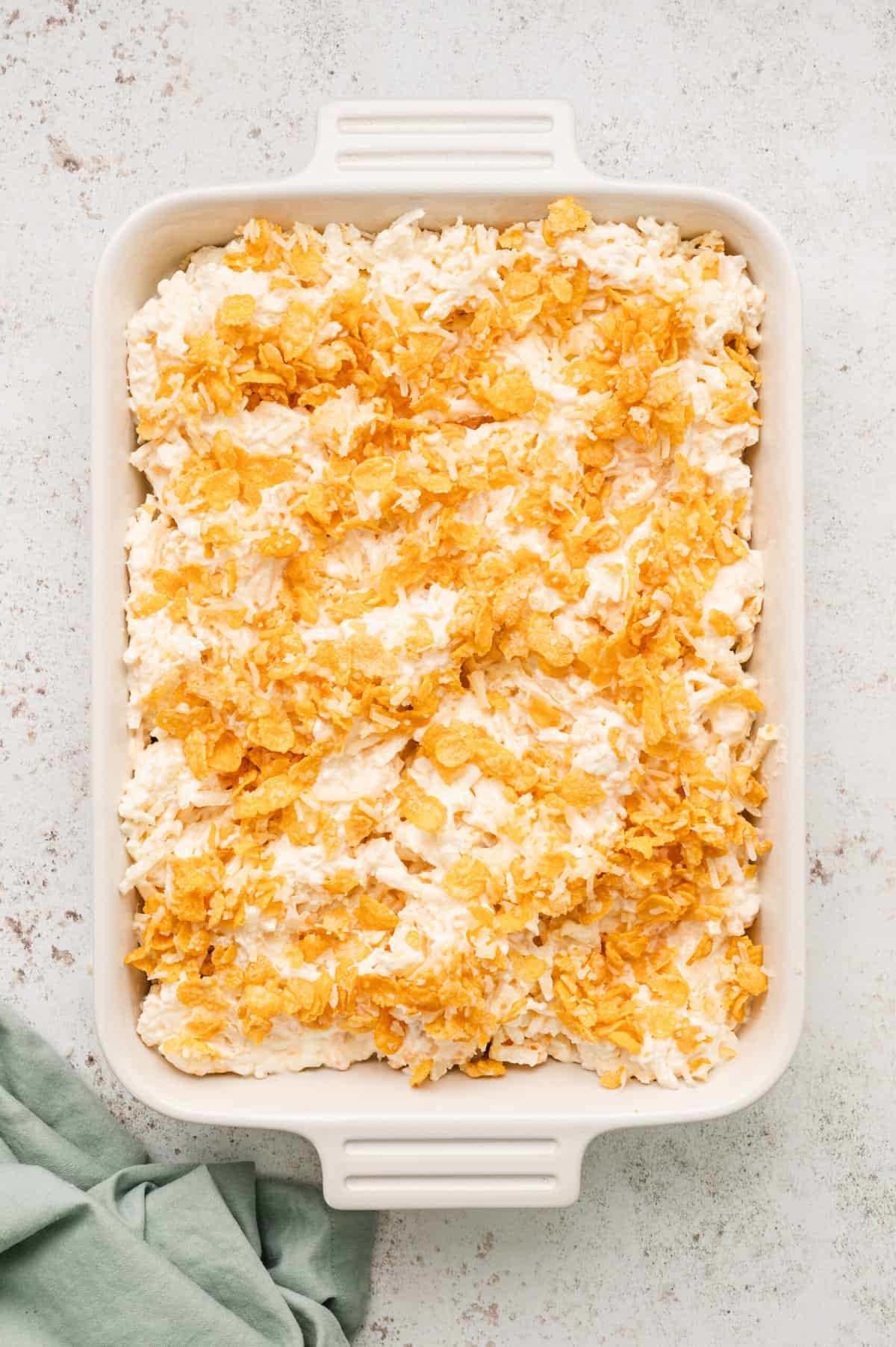 Topping the potato mixture with cornflake combination for Cornflakes, melted butter, and Parmesan cheese in glass mixing for Funeral Potatoes recipe
