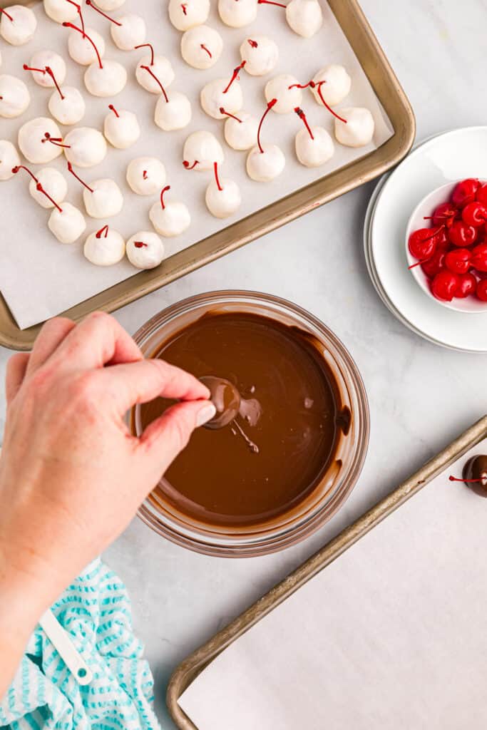 Dipping dough covered cherries in melted chocolate mixture of Chocolate Covered Cherries