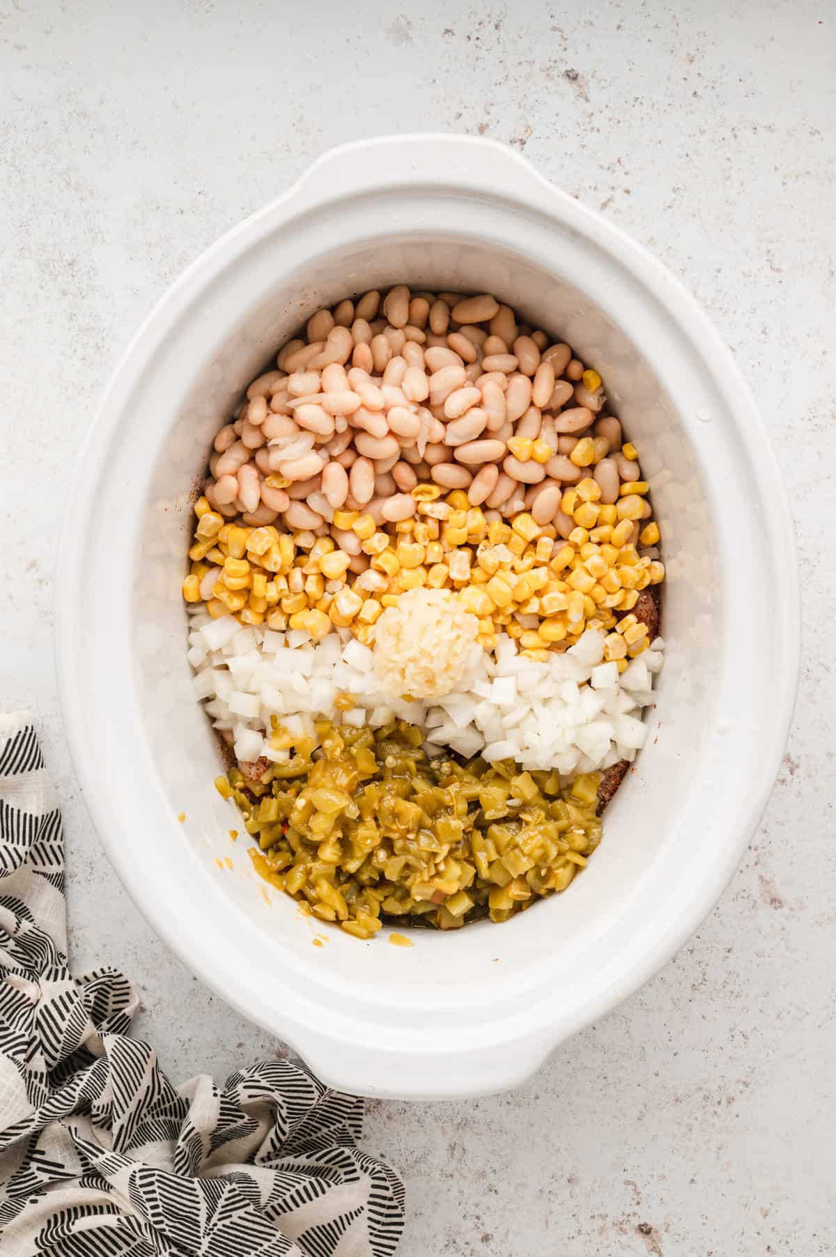 Adding beans, corn, onions, garlic, and chilis to crock pot for Slow Cooker White Chicken Chili