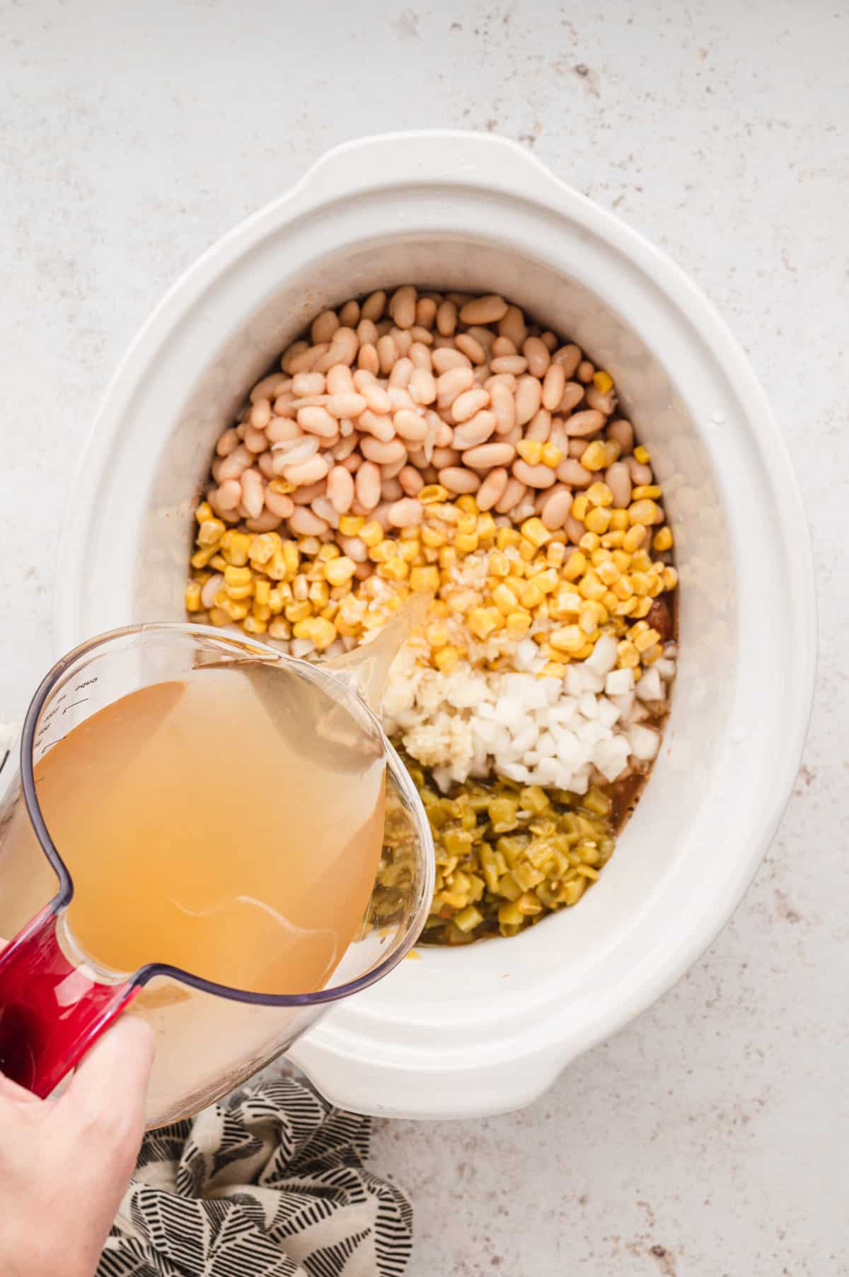 Pouring chicken broth atop Slow Cooker White Chicken Chili ingredients