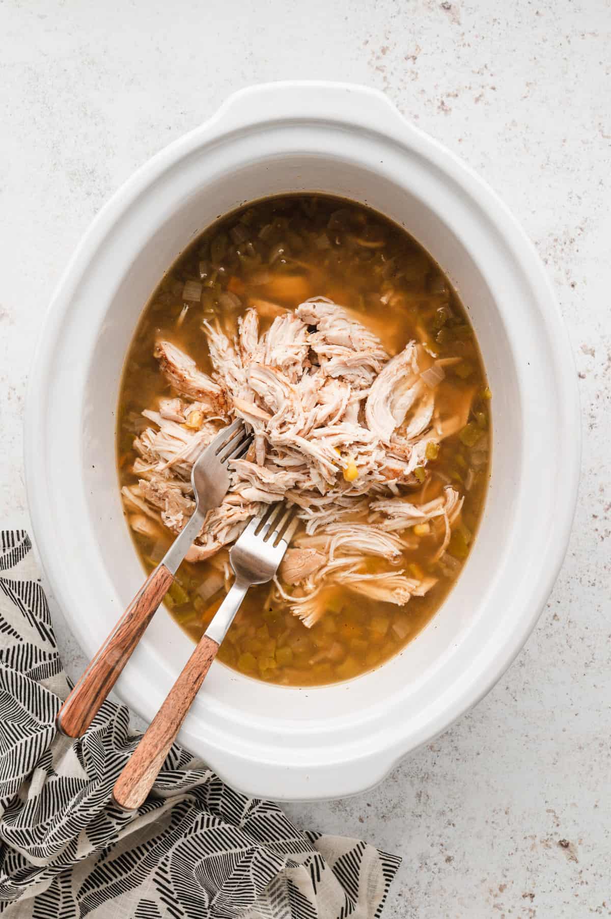 Removing chicken breasts from crock pot and shredding with two forks for Crock Pot White Chicken Chili recipe