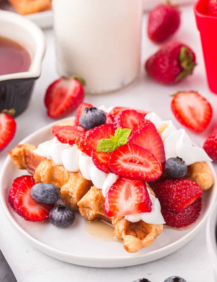 Plate full of croffles with whipped cream, strawberries and blueberries on top.