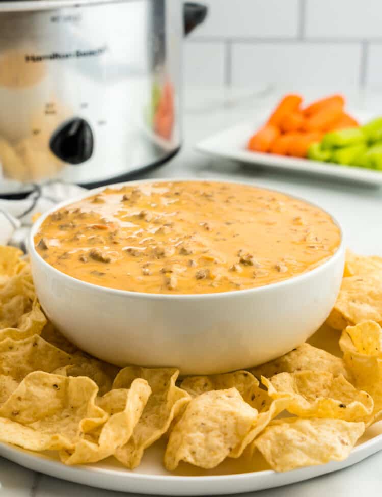 Crock Pot Hamburger Dip in Serving Bowl with Dippers and Crock Pot in Background