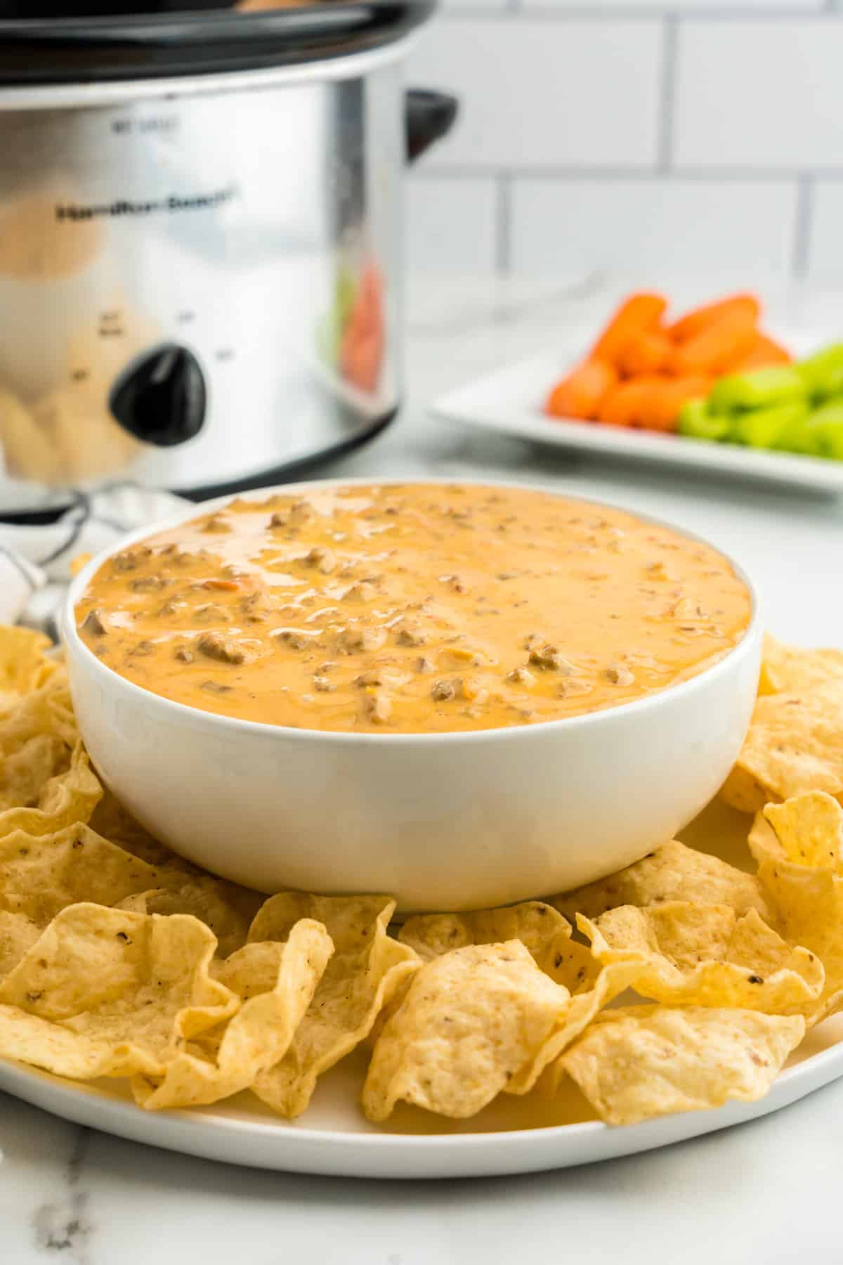 Crock Pot Hamburger Dip in Serving Bowl with Dippers and Crock Pot in Background