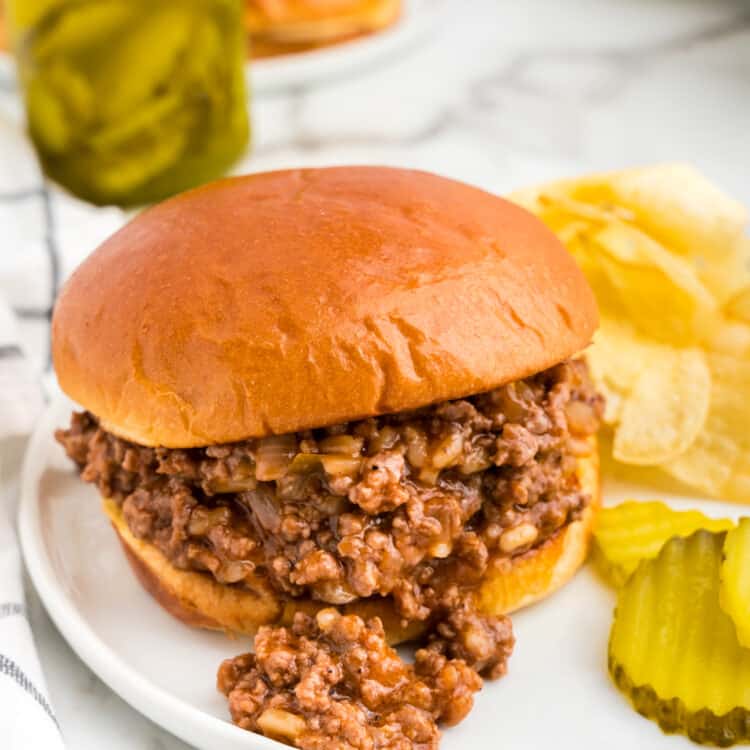 Large Batch Sloppy Joes recipe with meat on bun with chips and pickles on the side
