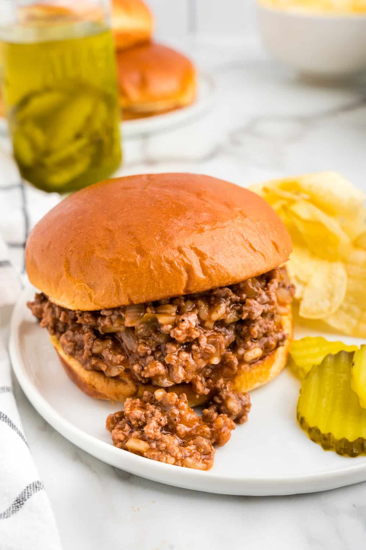 Large Batch Sloppy Joes recipe with meat on bun with chips and pickles on the side