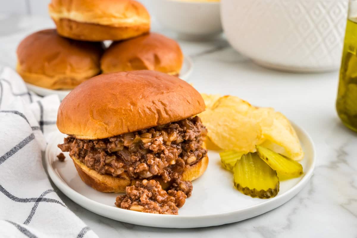 Sloppy Joe sandwhich on plate with pickles and potato chips