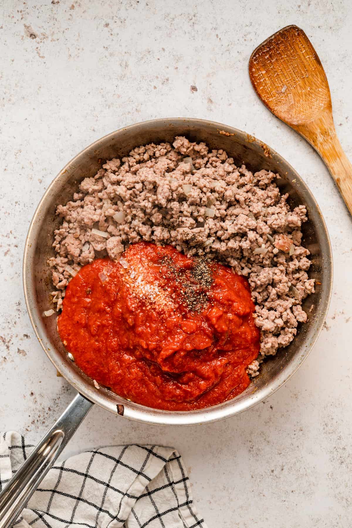 Adding tomato sauce and seasonings to browned sausage in stovetop skillet for Lasagna Casserole