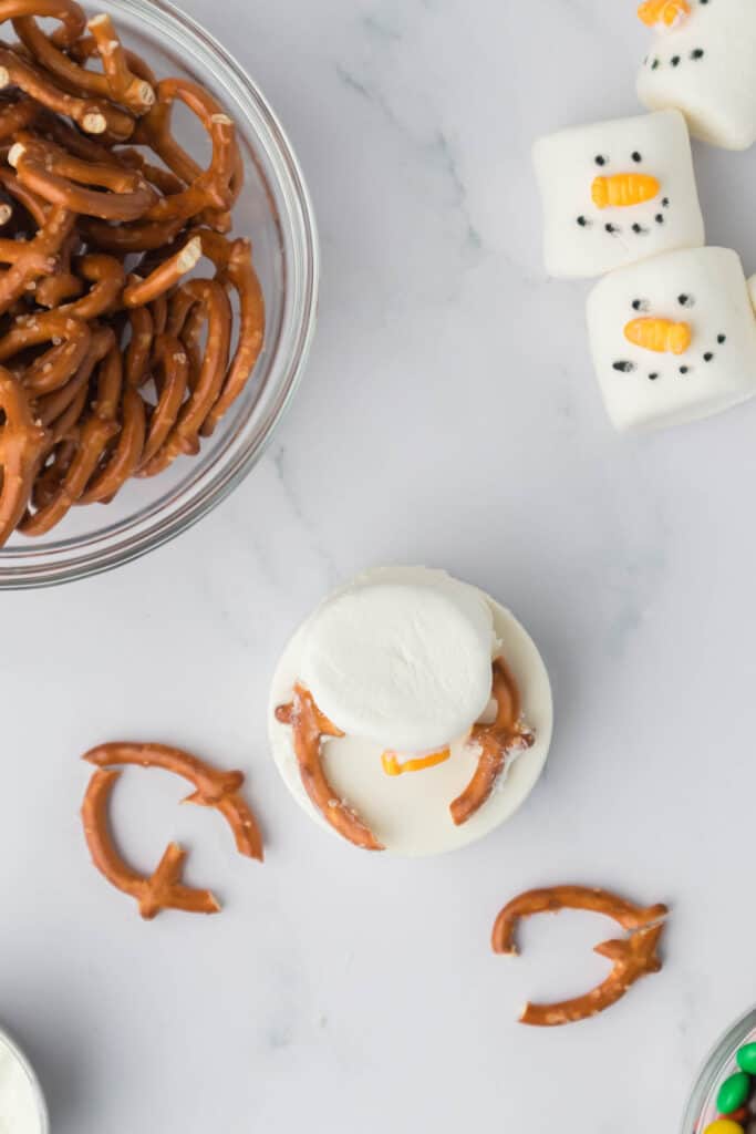 Break pretzels and attach them to the tops of the cookies with chocolate to resemble arms.