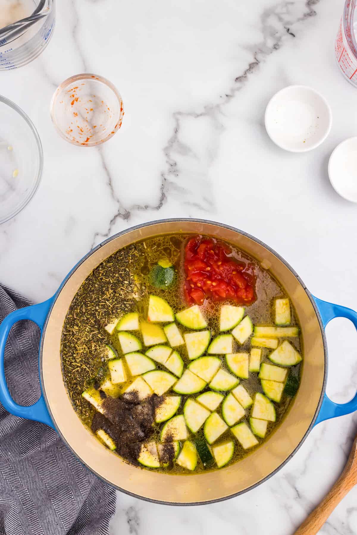 Adding zuchinni, spices, and tomato paste to Minestrone Soup ingredients in large pot