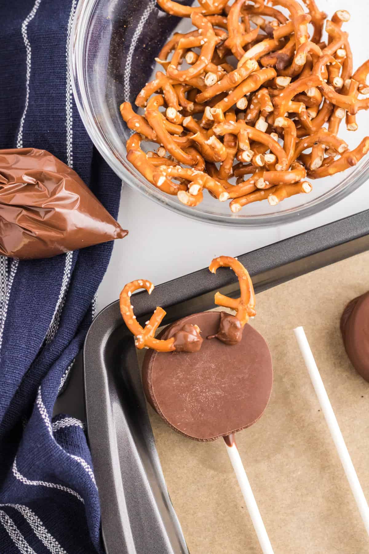 Place remaining Melted Chocolate in a Piping Bag and cut the End of it. Peel the Oreo Cookie Off of the Parchment paper and attache the Pretzels on the back with the remaining Melted Chocolate.